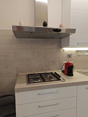 A kitchen with a stainless steel range hood, a gas stove, and a red kettle. - Apartment with a private pool and garden, just a few minutes from the beach (Pietrasanta)
