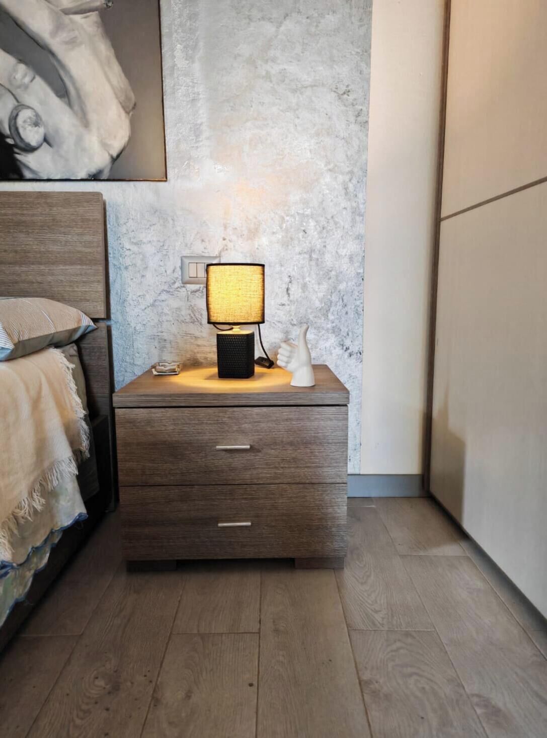 Ein Nachttisch aus Holz mit einer Lampe, einer Schublade und einem an der Wand befestigten Lichtschalter.