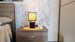 Uma mesa de cabeceira de madeira com uma lâmpada, uma gaveta e um interruptor fixado na parede.