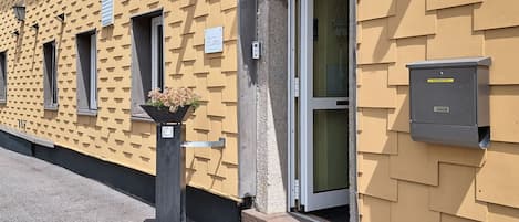 A building facade with a patterned exterior, a door with a glass panel, and a planter with flowers.