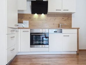 Una cocina moderna con armarios blancos, horno empotrado, lavavajillas y campana extractora negra.