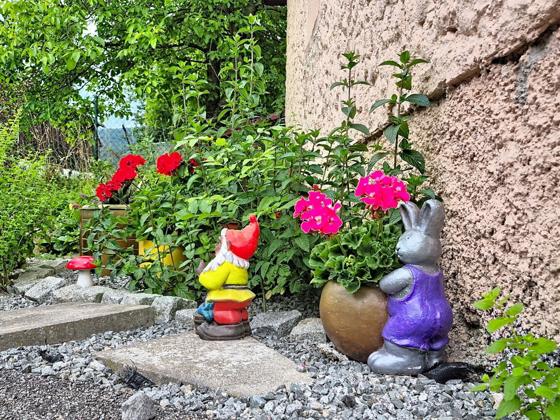 A garden with decorative statues, a potted plant with pink flowers, and a stone wall.