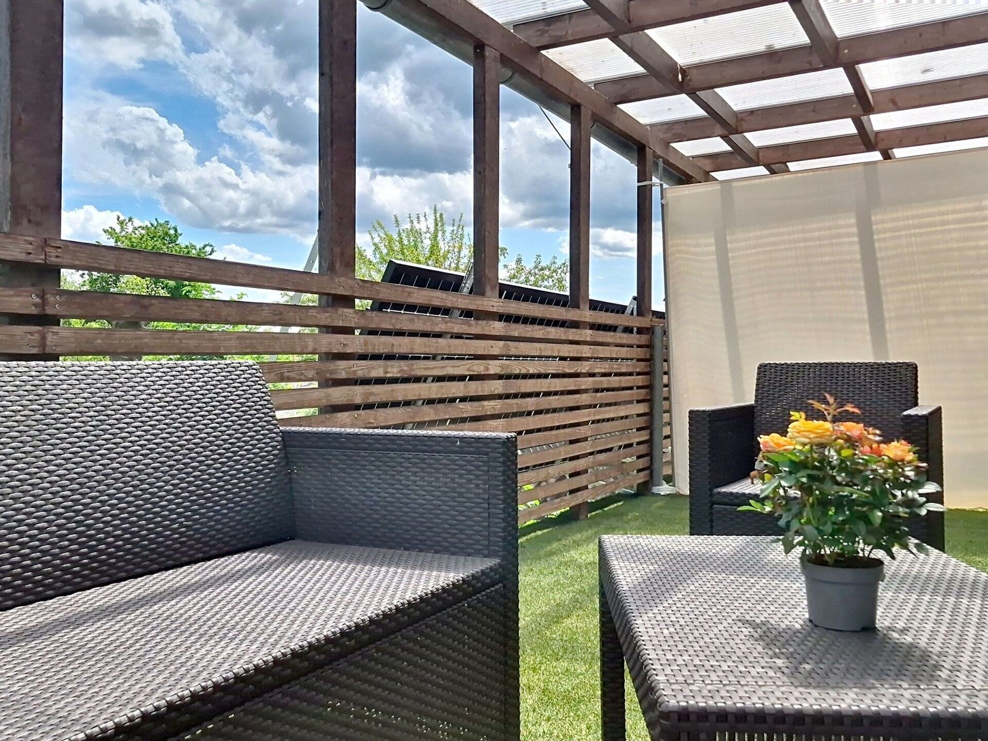 An outdoor patio with a wooden pergola, a wicker sofa, a small table, and a potted plant.