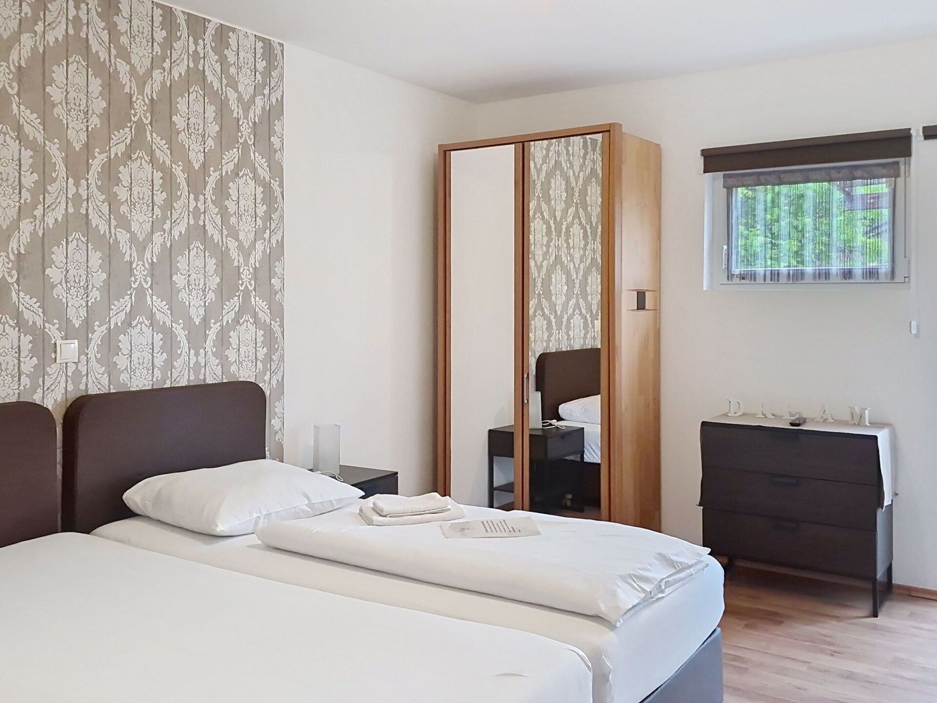 A hotel room with a bed, a wardrobe, a dresser, and a window with a view of trees.