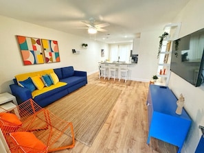 A modern living room with a blue sofa, a kitchen area, and a dining space. - NEW Gorgeous Sunshine-Up 6 Guests-Private Backyard (Port Orange)