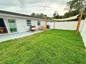 A backyard with a white fence, a picnic table, a grill, and a covered area. - NEW Gorgeous Sunshine-Up 6 Guests-Private Backyard (Port Orange)