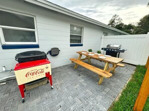 A backyard with a wooden picnic table, a Coca-Cola ice cooler, and a barbecue grill. - NEW Gorgeous Sunshine-Up 6 Guests-Private Backyard (Port Orange)