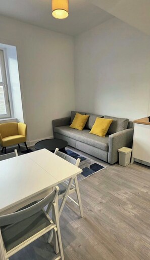 Ein modernes Wohnzimmer mit einem grauen Sofa, gelben Kissen, einem weißen Esstisch und einem kleinen runden Couchtisch.