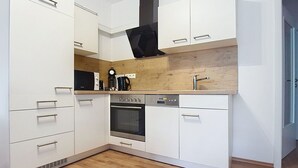 Una cocina compacta con muebles blancos, horno empotrado, cafetera y microondas.