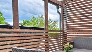Un patio exterior con listones de madera, dos sillas de mimbre, una mesita y una planta en maceta.