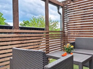 Une terrasse extérieure avec des lames de bois, deux fauteuils en osier, une petite table et une plante en pot.