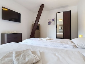 Una habitación de hotel moderna con cama, televisor de pantalla plana en la pared, armario y un espejo grande.