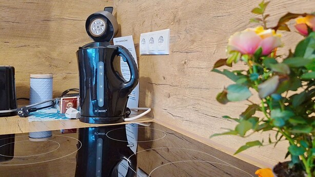 Una cocina con cafetera, hervidor y una planta.