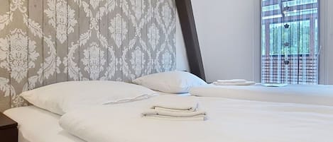 Et hotelværelse med to senge, hvide sengetøj, tapet med mønster og et vindue med udsigt til træer.