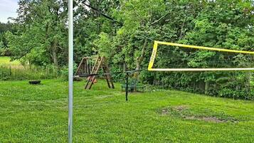 En græsplæne med volleyballnet, en metalstang og en træstige.