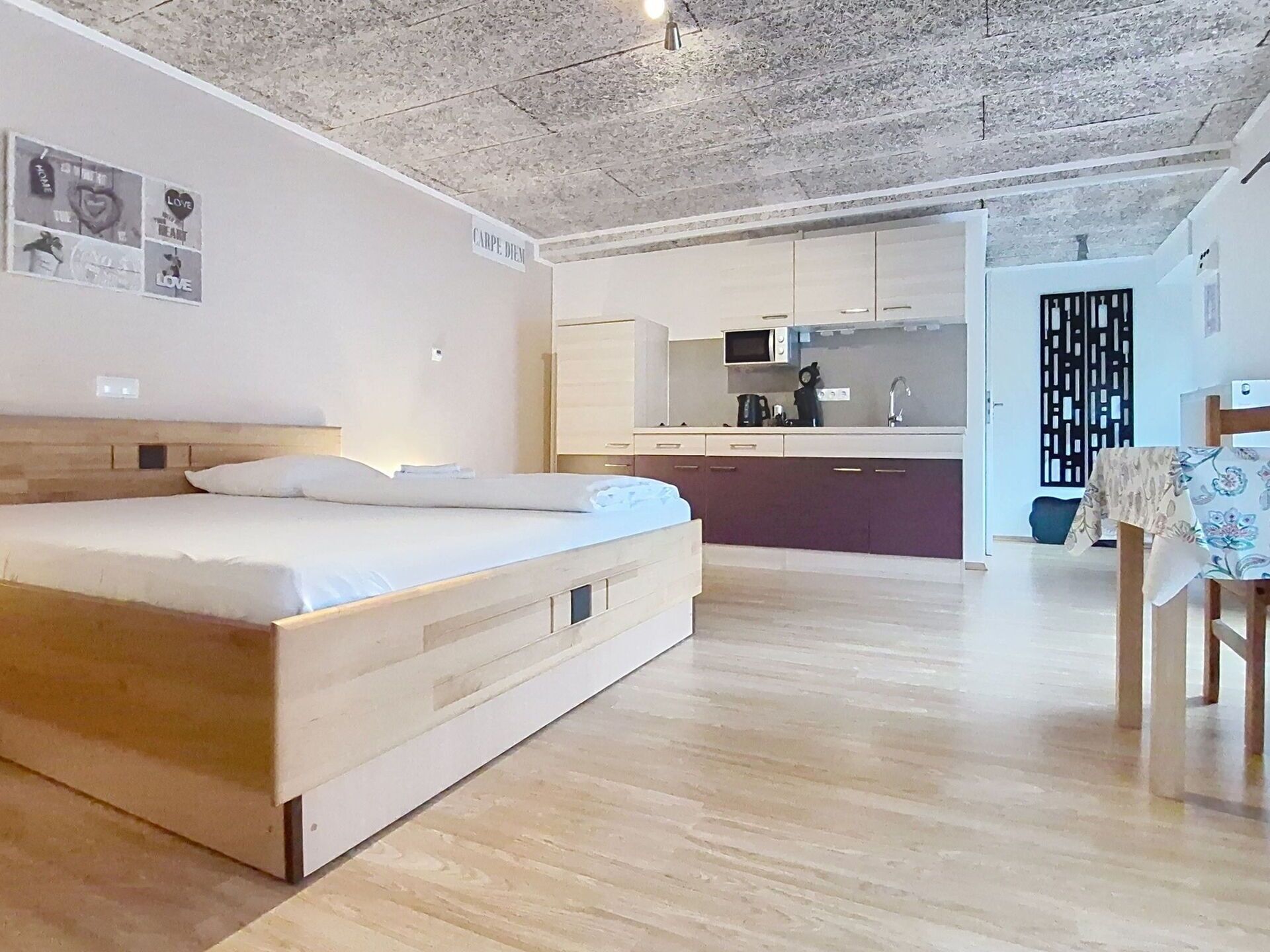 A bedroom with a wooden bed, a kitchenette, and a dining area.