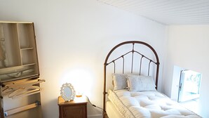 Um quarto com cama, mesa de cabeceira, cômoda e prateleira na parede.