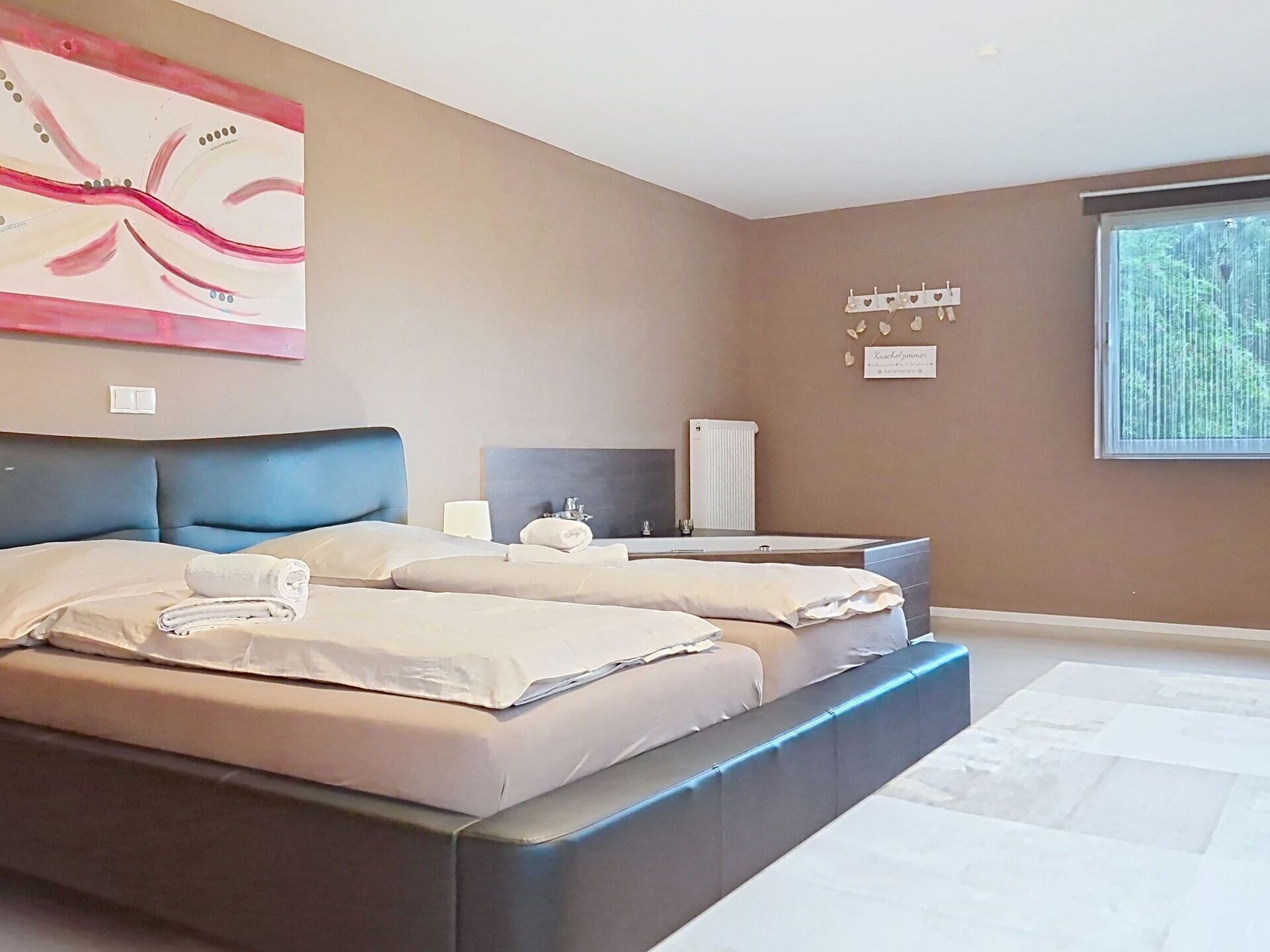A modern bedroom with a large bed, bedside tables, a mirror, and a window with a view of trees.