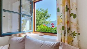 A room with a large window, a sofa, and a view of greenery and flowers.