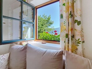 A room with a large window, a sofa, and a view of greenery and flowers.