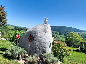 A large rock with a carved owl and sun design, surrounded by greenery and a clear sky.