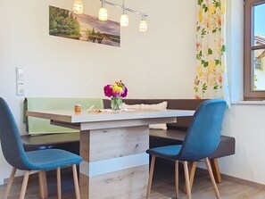 A dining area with a wooden table, two blue chairs, a vase with flowers, and a painting on the wall.