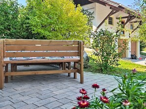 A wooden bench with a cushion, surrounded by greenery and a paved area. - Beautiful apartment for 4 guests with WIFI, TV and terrace (Oberwang)