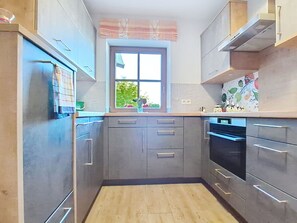 A compact kitchen with grey cabinets, a window, and a built-in oven.