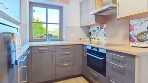Une cuisine moderne avec des meubles gris, un four encastré et une fenêtre donnant sur un paysage verdoyant.