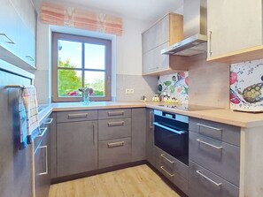 A modern kitchen with grey cabinets, a built-in oven, and a window with a view of greenery. - Beautiful apartment for 4 guests with WIFI, TV and terrace (Oberwang)