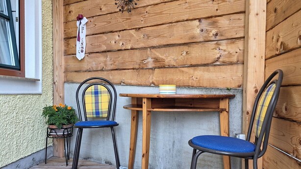 A wooden exterior wall with a window, two chairs, a table, and a patterned rug.