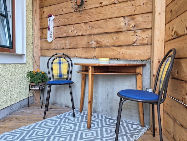 A wooden exterior wall with a window, two chairs, a table, and a patterned rug.