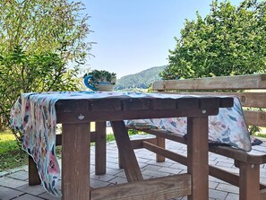 An outdoor wooden table with a floral tablecloth, a potted plant, and a bench in a garden setting.