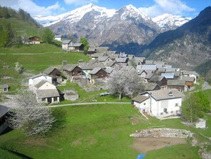 Uma aldeia com casas tradicionais, um pequeno lago e montanhas cobertas de neve ao fundo.
