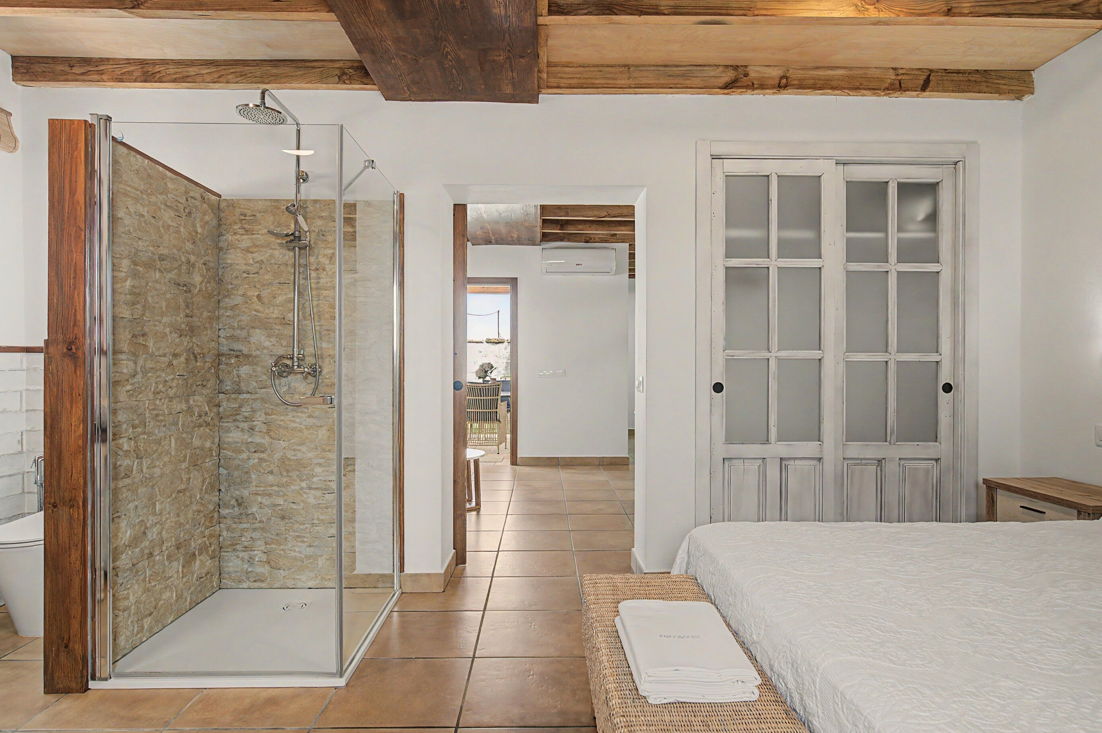 A bedroom with a bed, a glass-enclosed shower, and a wooden door.