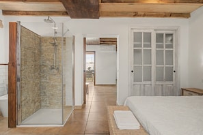 Ein Schlafzimmer mit einem Bett, einer Glaskabine zur Dusche und einer Holztür.