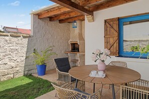Eine Terrasse mit einem runden Holztisch, Korbstühlen, einem Blumentopf und einer Steinmauer.