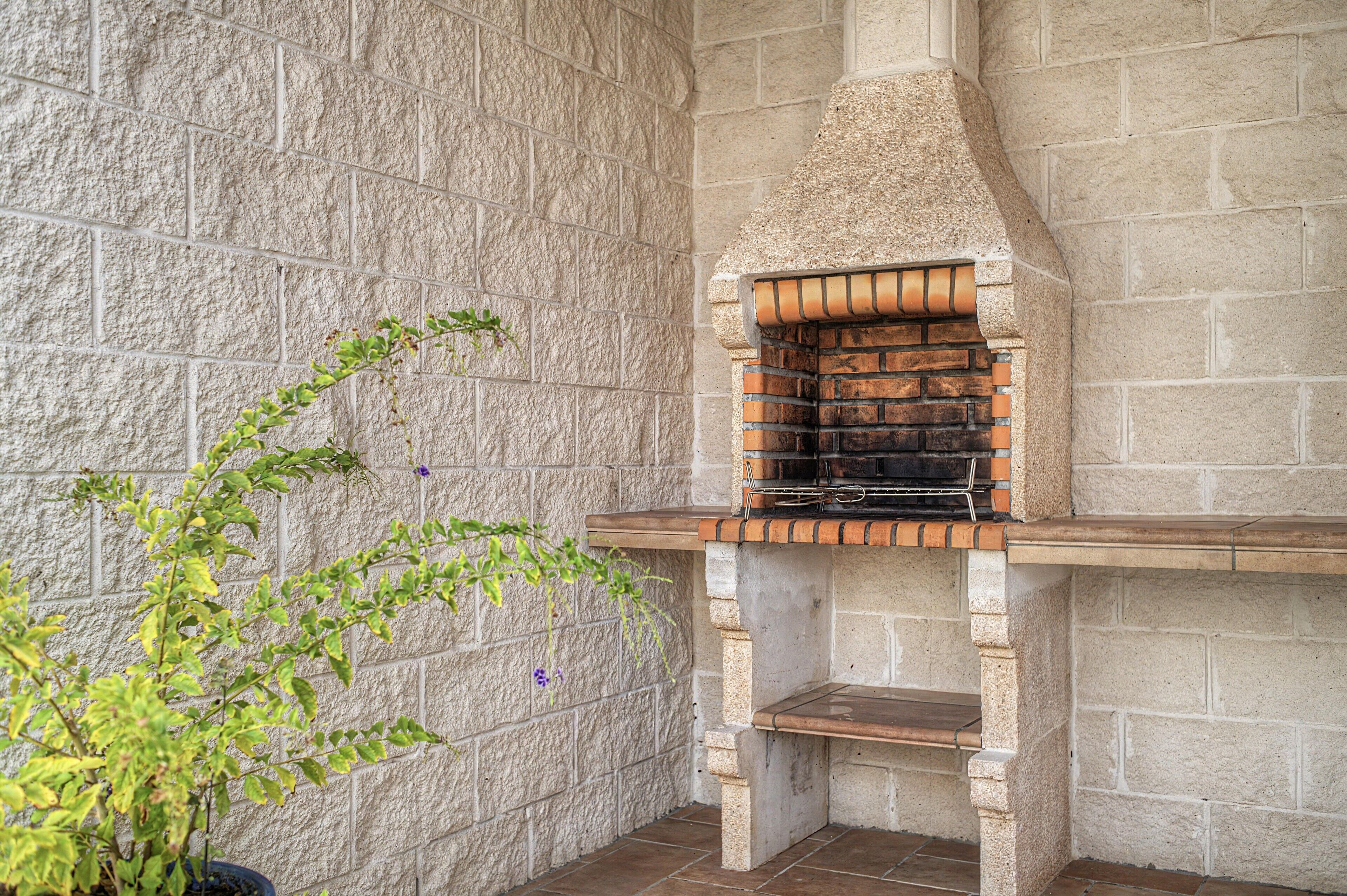 Un four extérieur en pierre, avec un intérieur en briques, une étagère en bois et une plante en pot placée à côté.