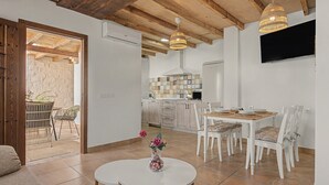 Una cocina moderna con armarios blancos, una zona de comedor con sillas blancas y un televisor montado en la pared.