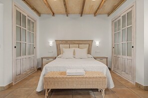 A bedroom with a wooden headboard, white bedding, two bedside tables, and a wicker bench. - Tartesos 6 with private pool, Wi-Fi and air conditioning (Conil de la Frontera)