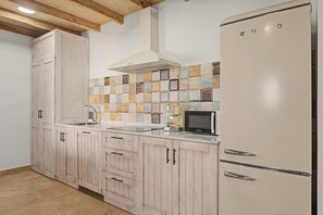 Eine Küche mit Holzausstattung, einer gefliesten Spritzschutzwand, einer eingebauten Mikrowelle und einem Kühlschrank.