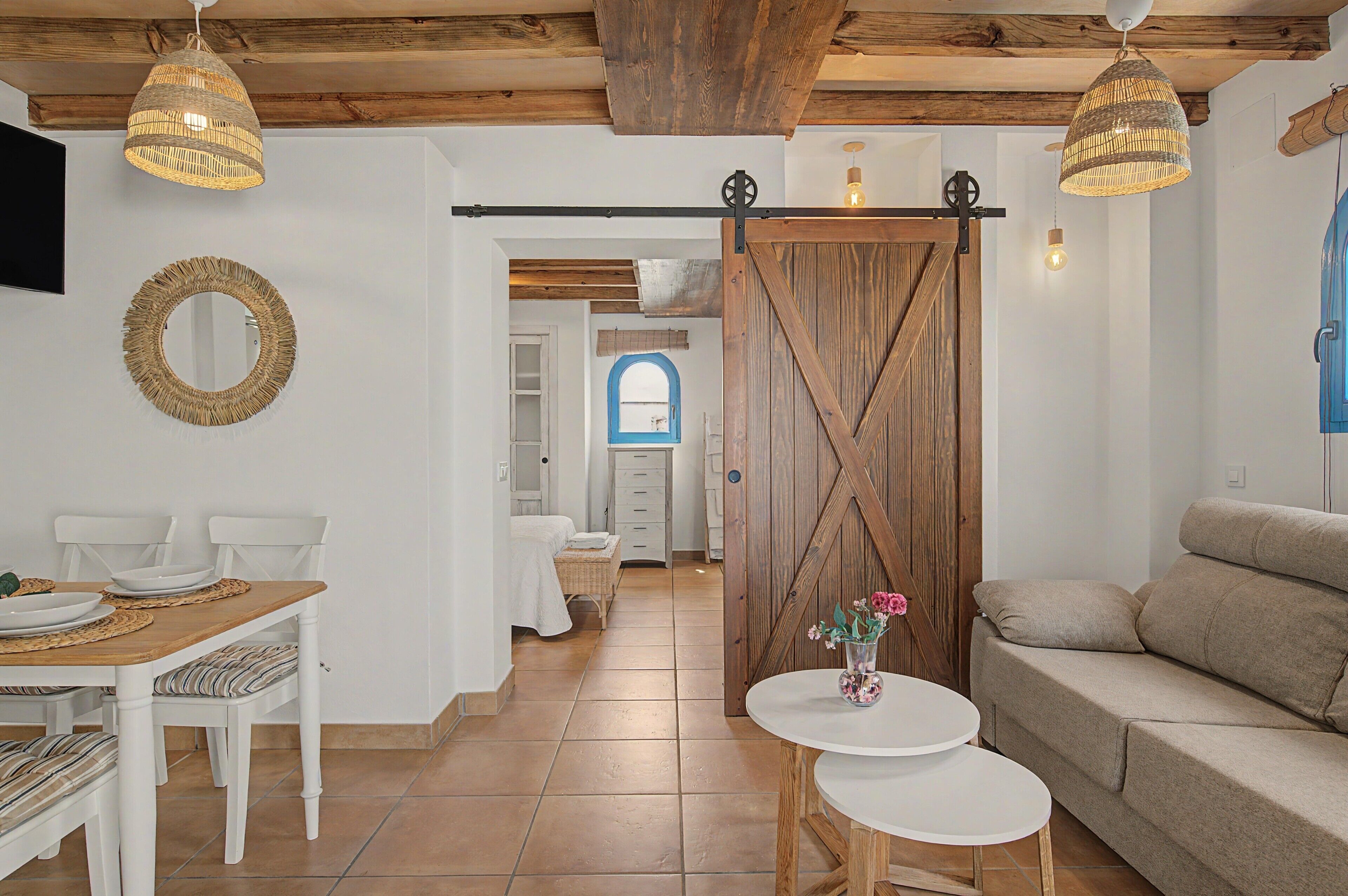 A room with a dining table, chairs, a sofa, and a small round table with a vase.