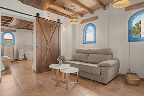 A cozy room with a wooden door, a sofa, a small table, and a window with a view.