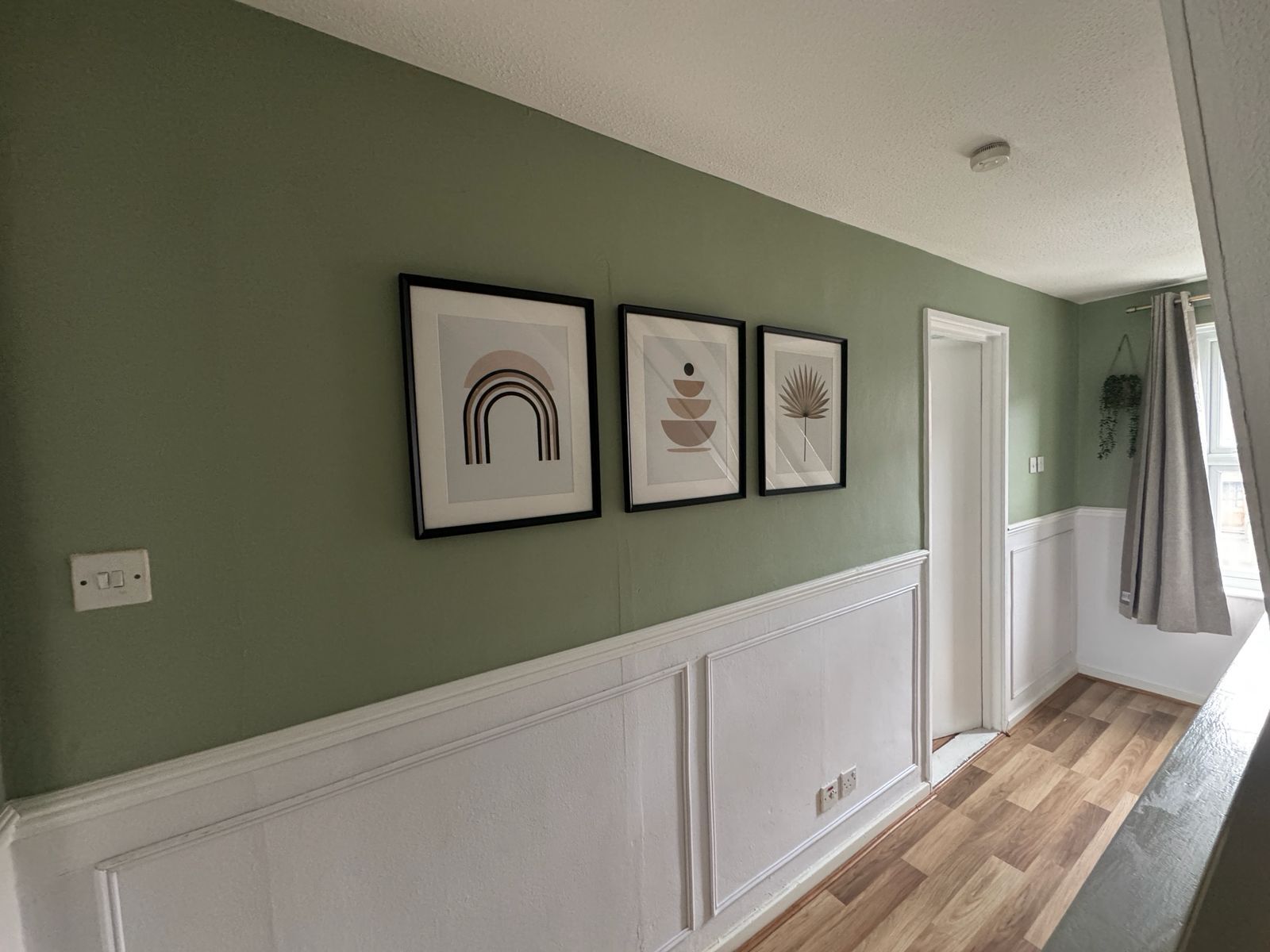 A hallway with a green wall, white wainscoting, and framed artwork.