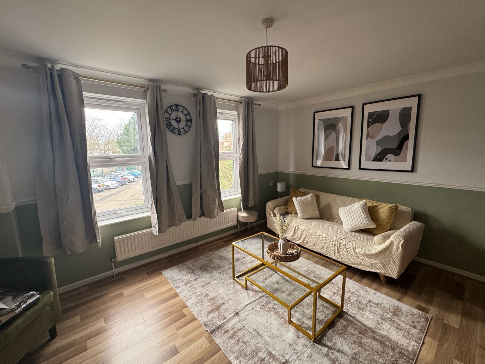A living room with a sofa, a coffee table, a clock, and two framed pictures on the wall.