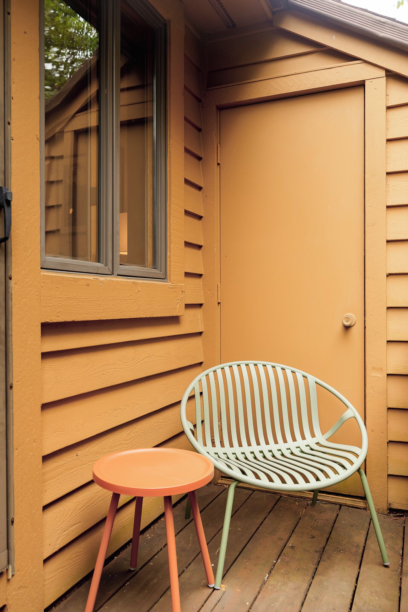 Una esquina de un edificio con una ventana, una puerta y un pequeño espacio exterior con una silla y una mesa.