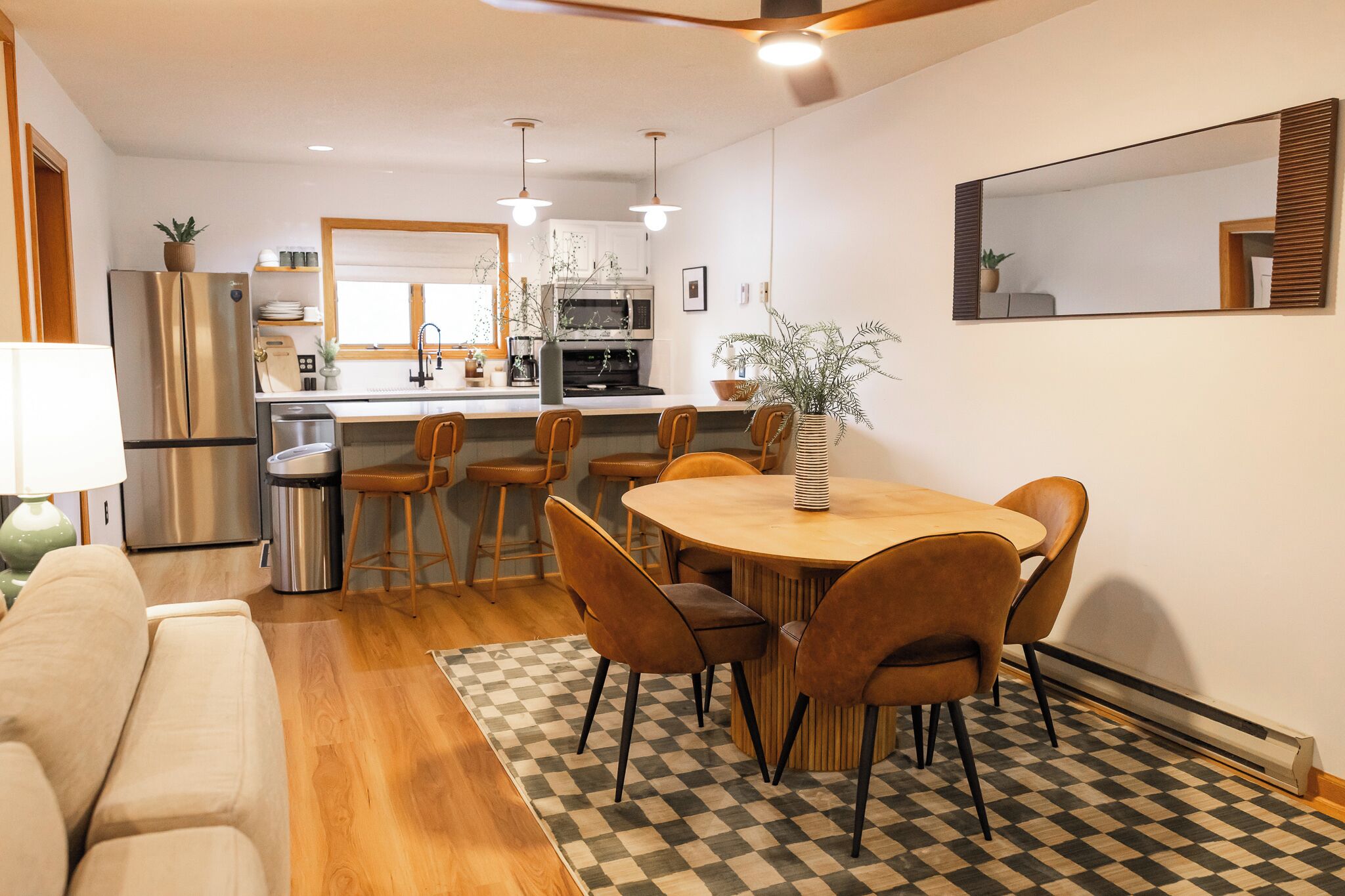 A modern kitchen with a central island, a dining area with a round table and chairs, and a living area with a sofa.