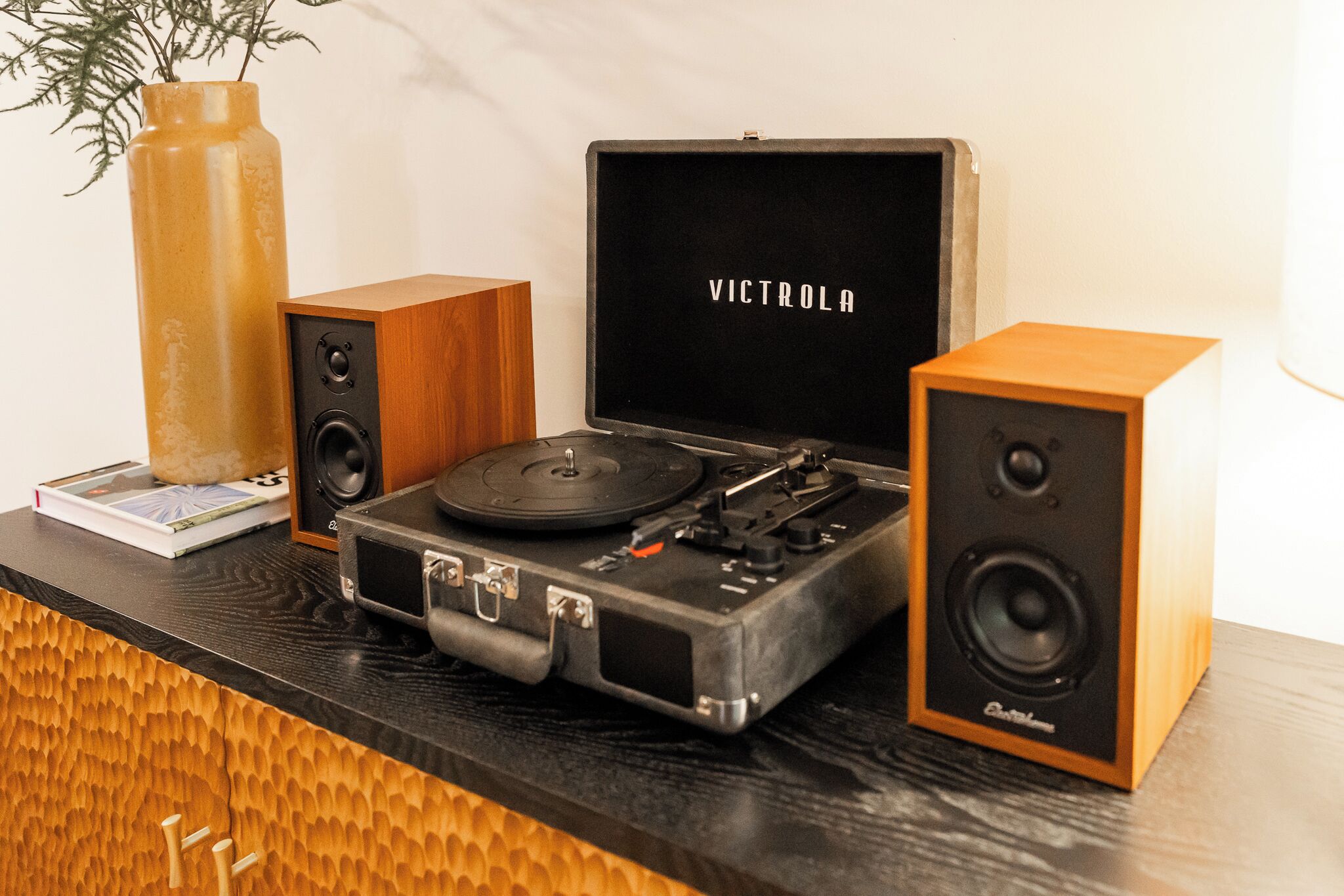 A turntable with a vinyl record, a speaker, and a box labeled 'VICTROLA' on a wooden surface.