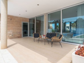 Une terrasse ensoleillée avec une porte vitrée donnant sur un espace piscine, aménagée avec des fauteuils en osier et une petite table.
