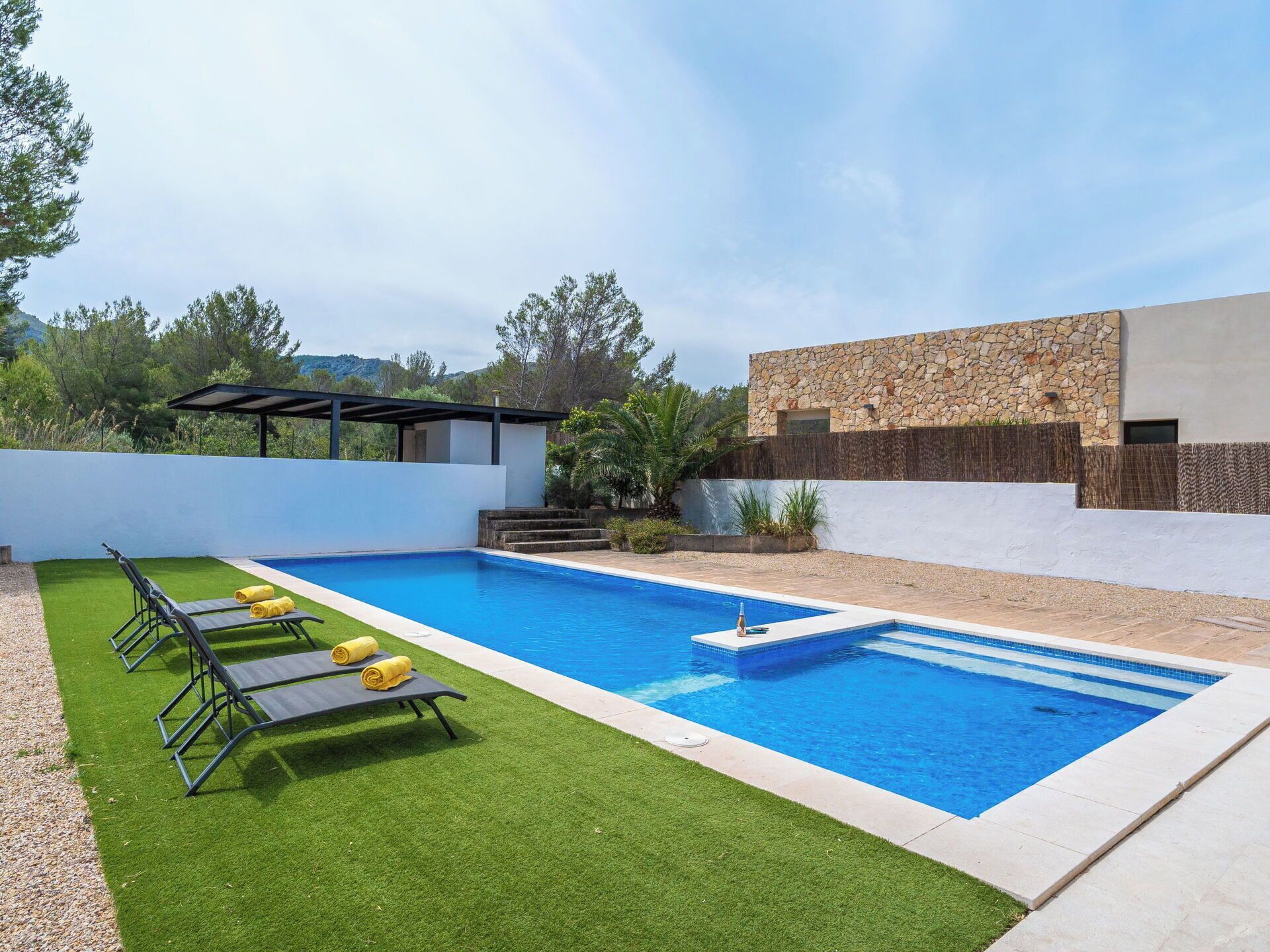 A swimming pool with a modern design, surrounded by artificial grass and a stone wall.